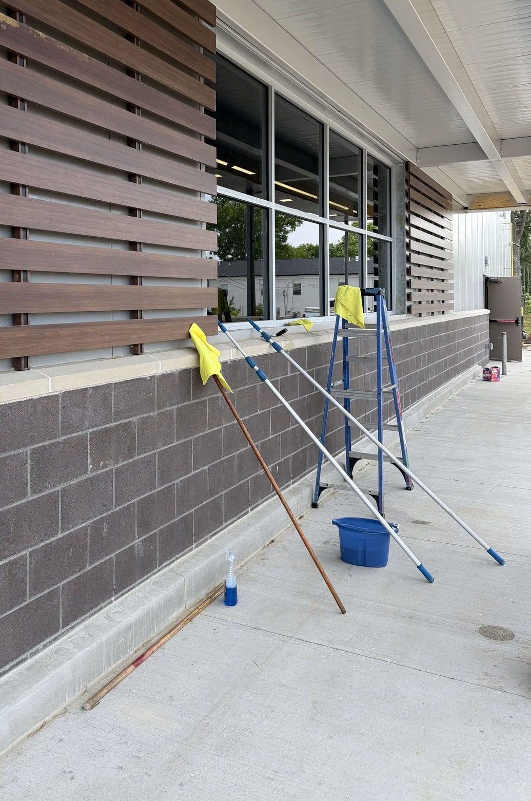 Storefront windows with window-cleaning poles, a squeegee, a bucket and a ladder set up on the sidewalk