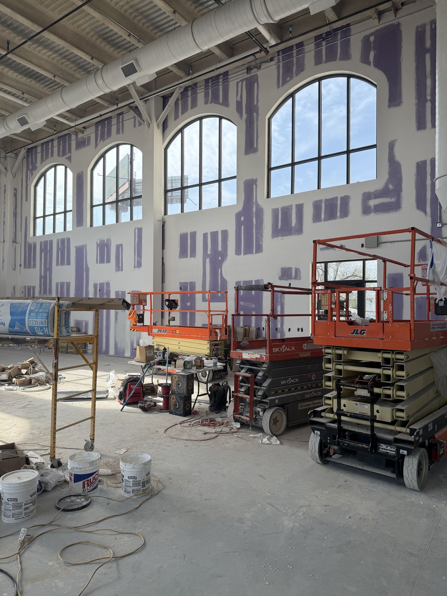 Large interior under construction with arched windows and scissor lifts